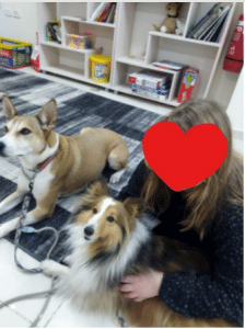 Girl with face covered by heart emoji patting two dogs inside on the carpet