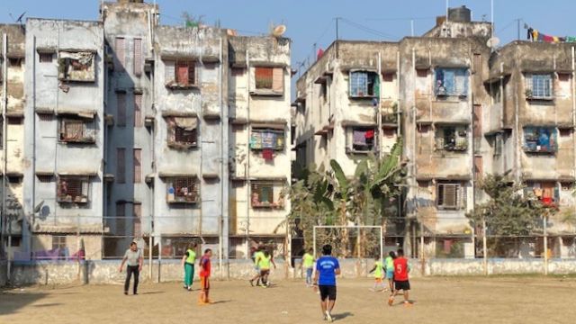 India students playing soccer in a field with old, multistory buildings behind